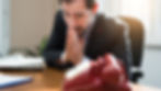 Anxious man in a suit sitting at a desk, staring at a red rotary phone with hands clasped in worry — symbolizing emotional tension, waiting, or fear of confrontation, relevant to themes of vulnerability and pretending in daily life.
