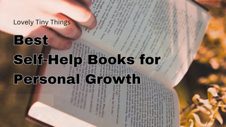 Hand holding an open book with blurred text overlay: "Lovely Tiny Things, Best Self-Help Books for Personal Growth" in bold black font. Warm background.