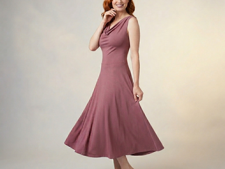 A smiling redhead model posing barefoot in a sleeveless mauve rose Nicole midi dress made from soft bamboo cotton jersey, featuring a draped cowl boatneck neckline and a fluid A-line flare hem.