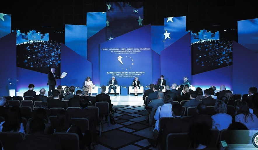 Conference speakers in front of a blue geometric stage set.