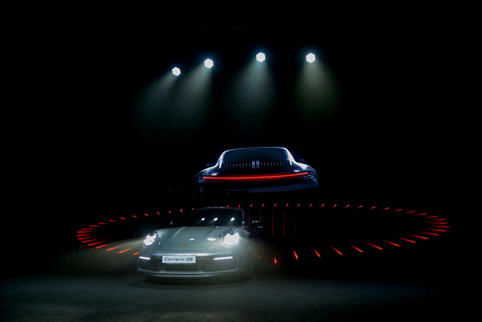 Porsche 911 reveal beneath spotlights and a circular floor installation.