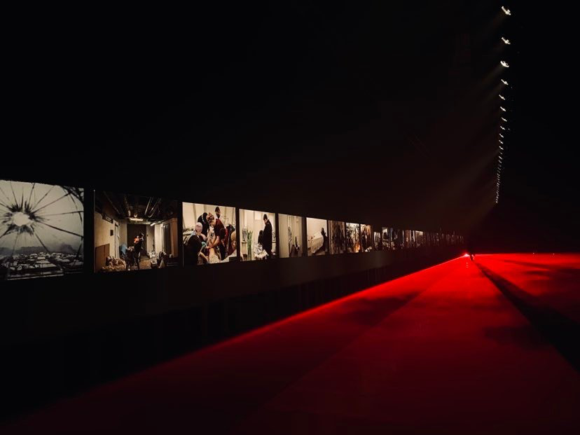 Photographic works in a dark gallery with a red-lit walkway.