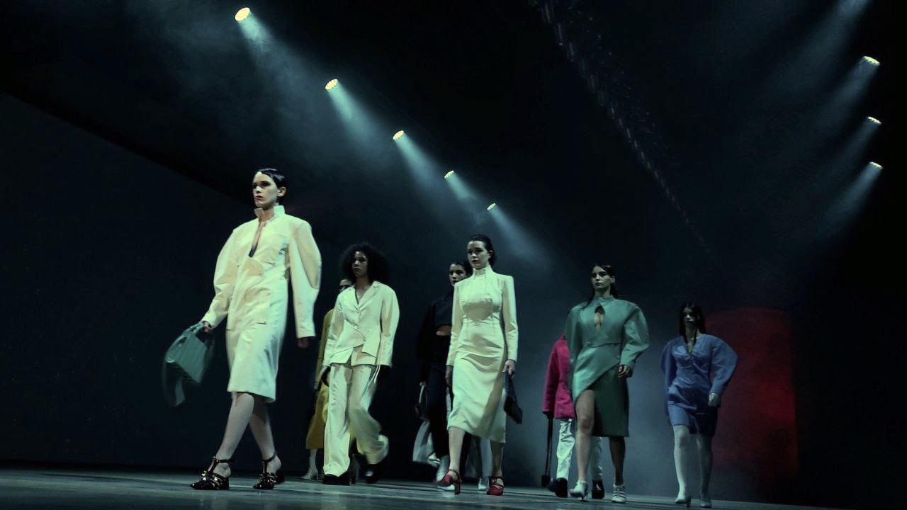 Models on the runway beneath focused stage lighting.
