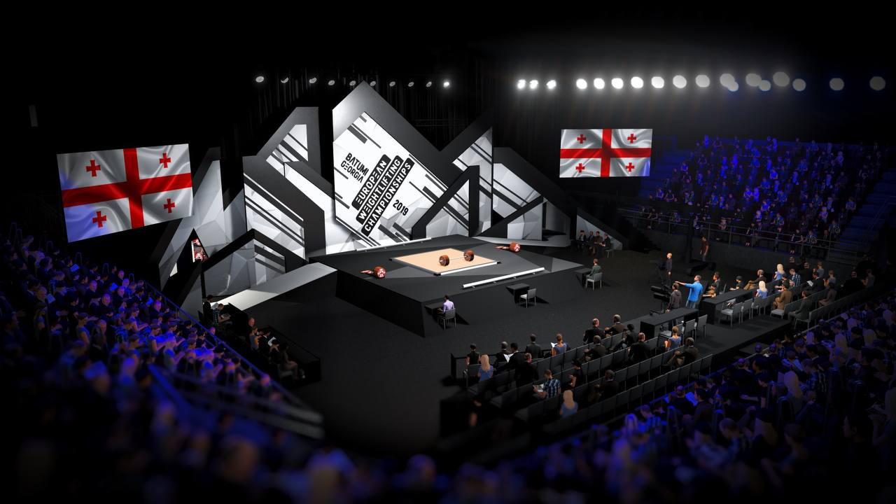 Weightlifting venue with geometric stage screens and Georgian flags.
