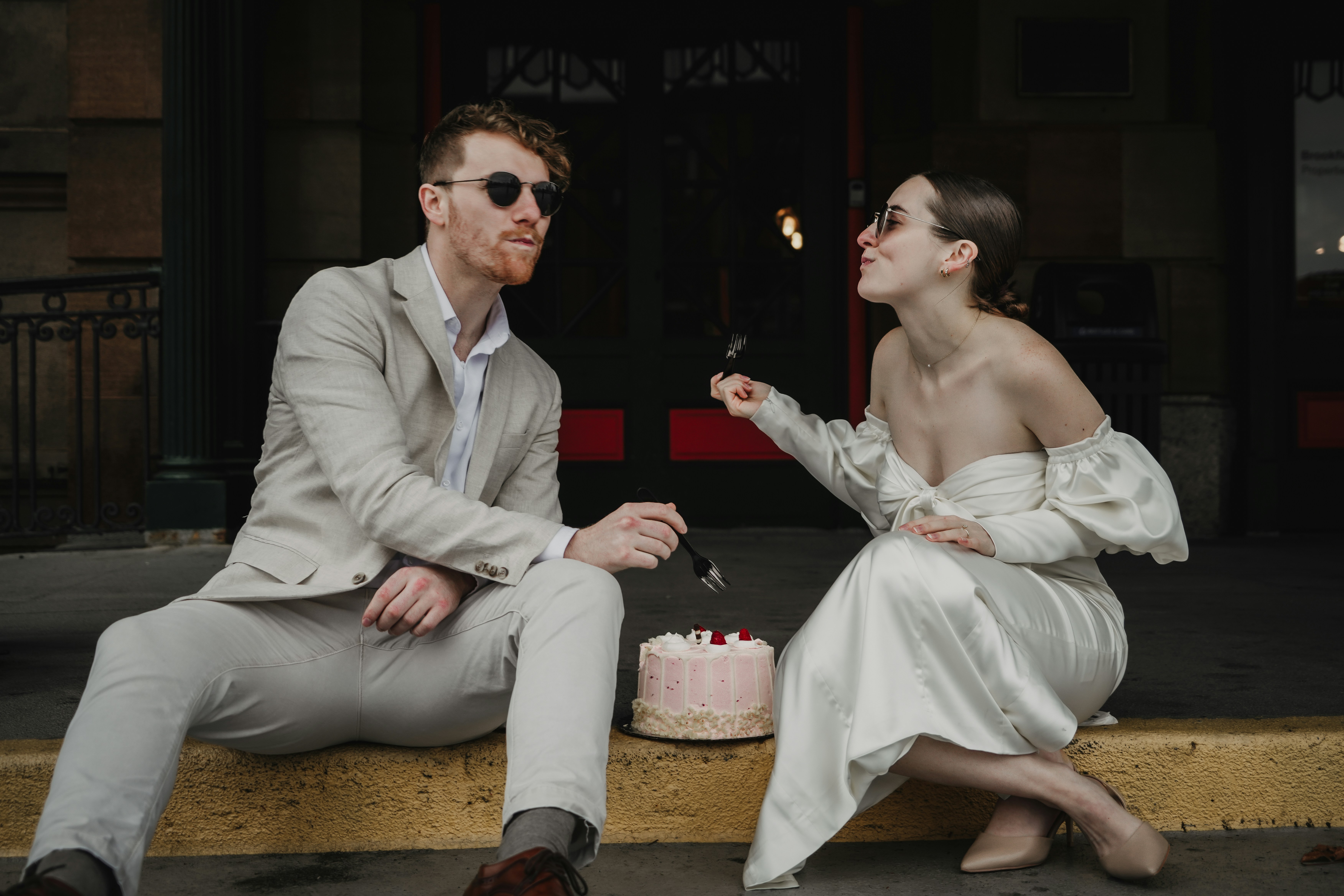 couple in wedding attire eating cake on the side of road in Pittsburgh