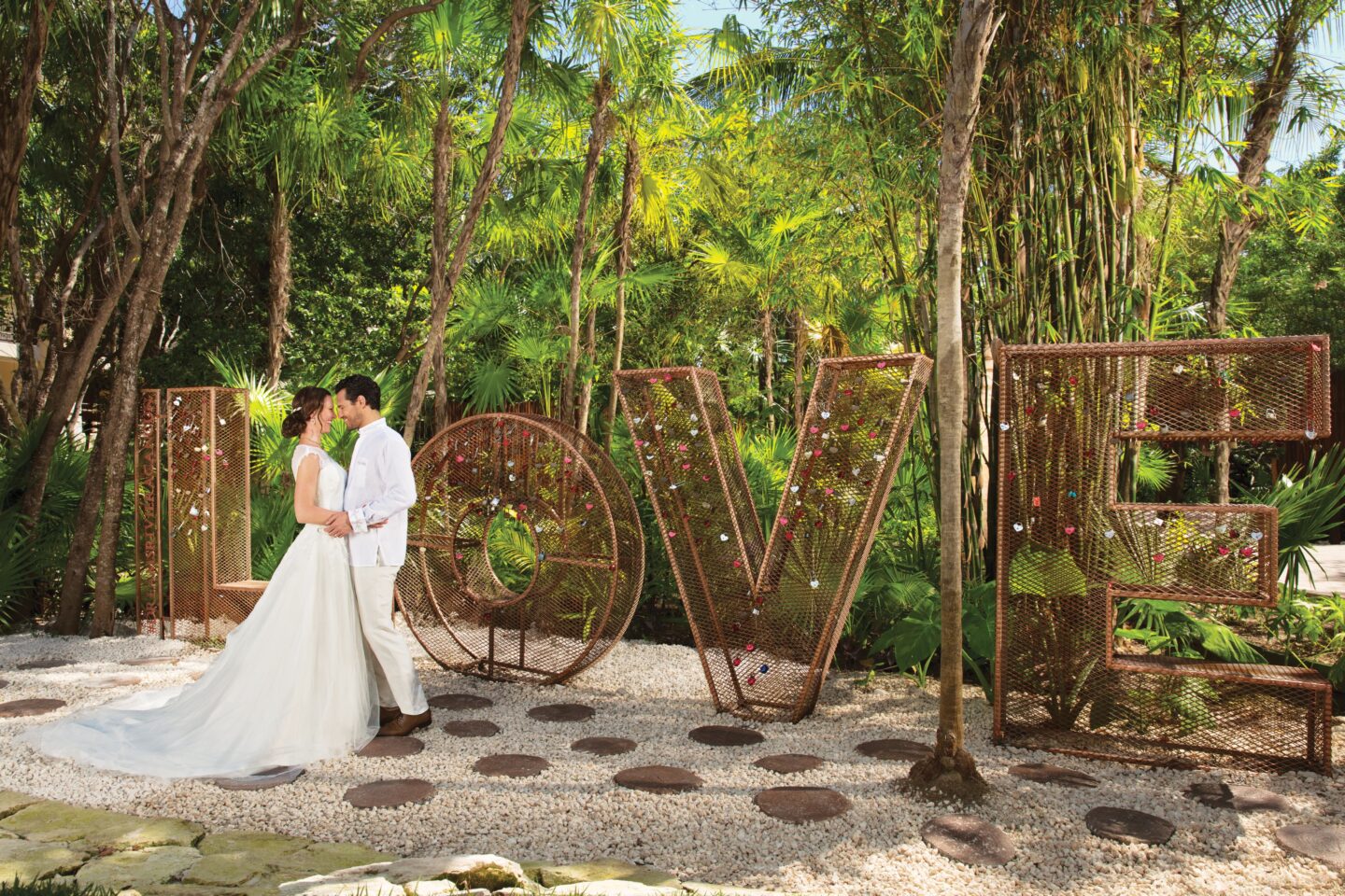 couple in wedding attire embrace next to LOVE sculpture