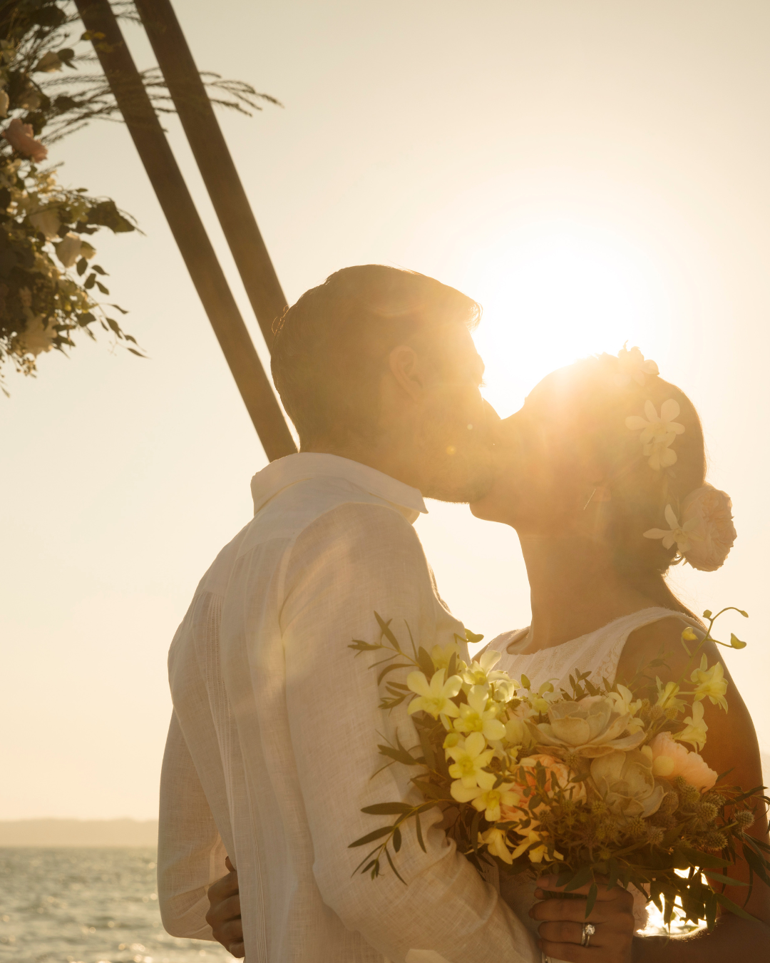 couple kissing in wedding attire with sunlight behind them