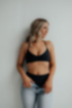 Woman in a black bikini standing confidently against a white wall, highlighting smooth post-laser results