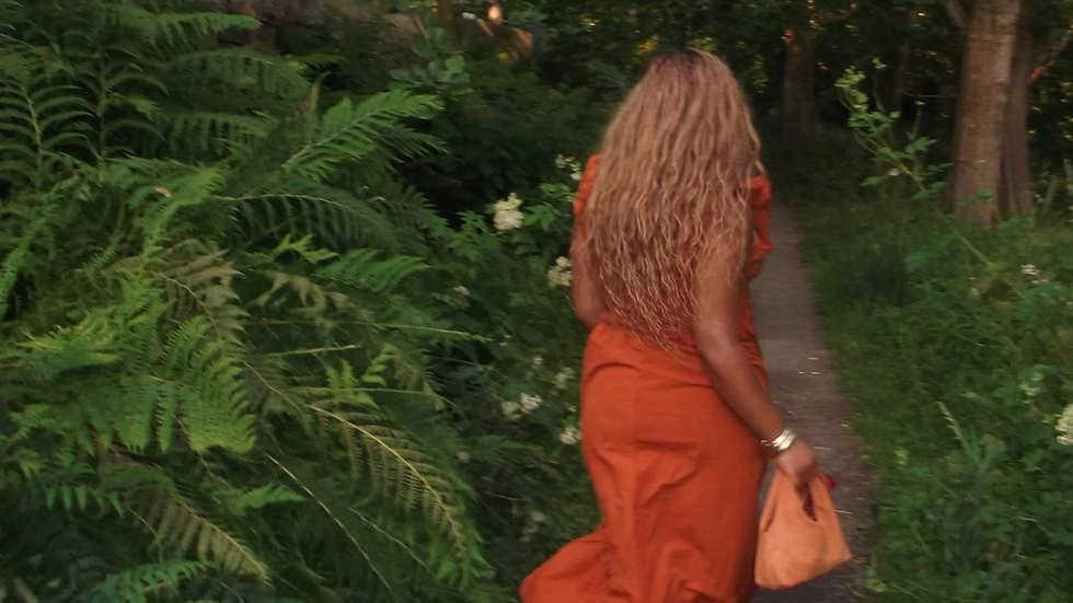 Woman in an orange dress walking through a green forest path