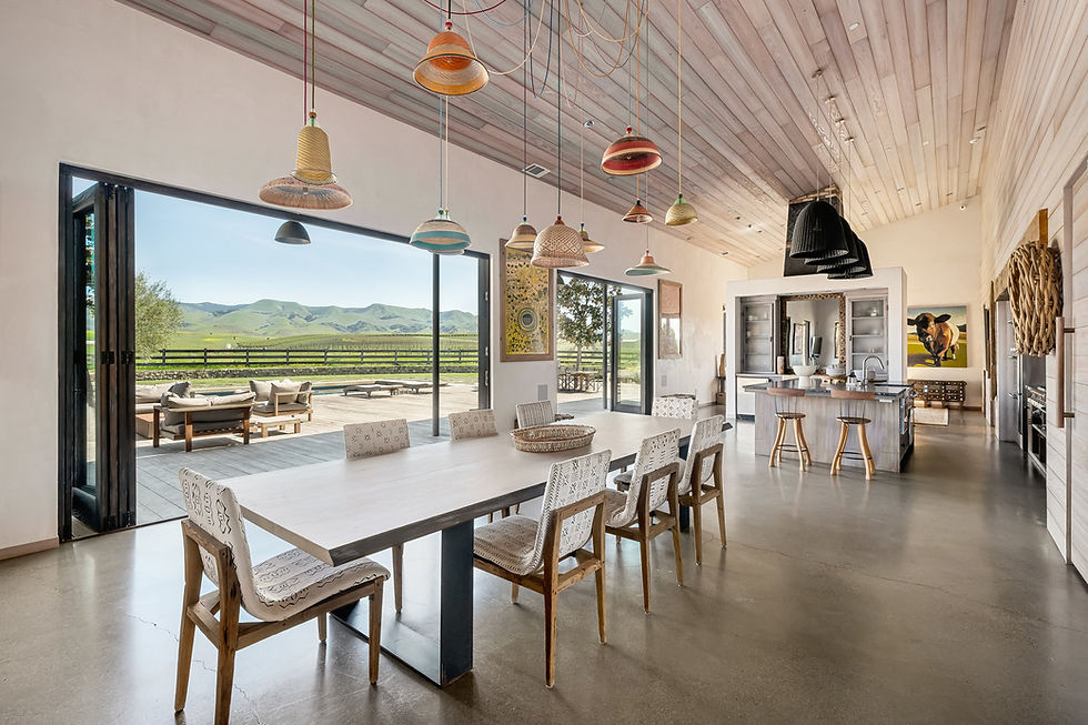Open great room with wide glass doors folded back to a deck and green fields