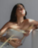 Woman with tattoos relaxes in sunlight, eyes closed, leaning on a white surface. Wears a ribbed top and jewelry, serene