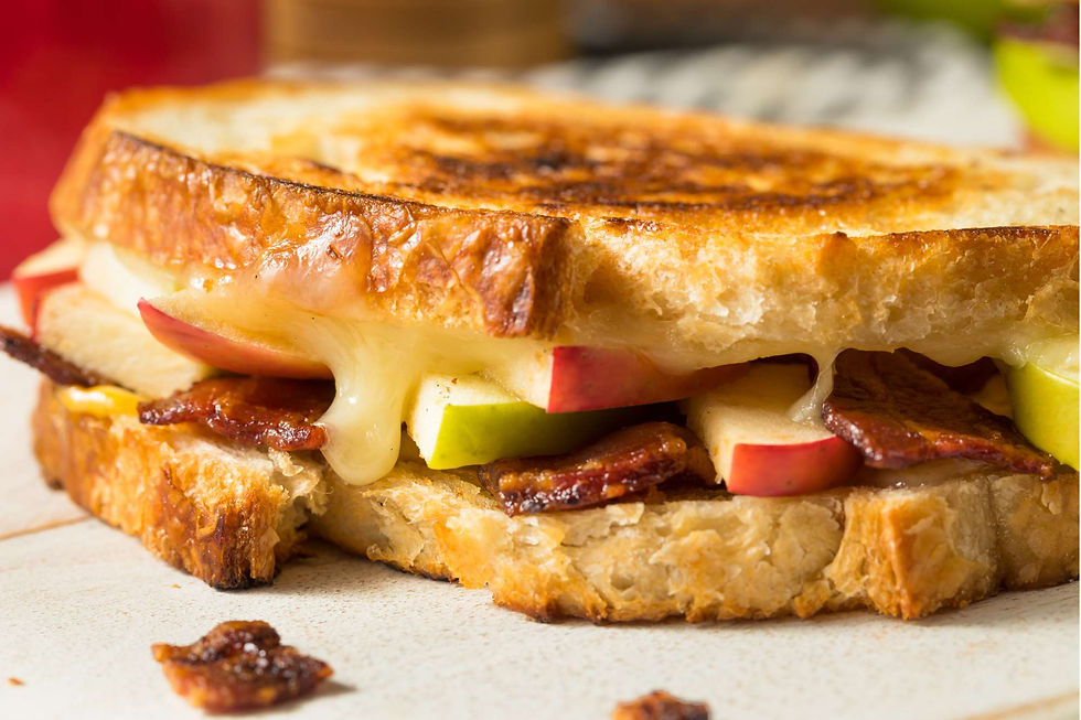 Grilled cheese sandwich with melted cheese, green and red apples, and bacon.