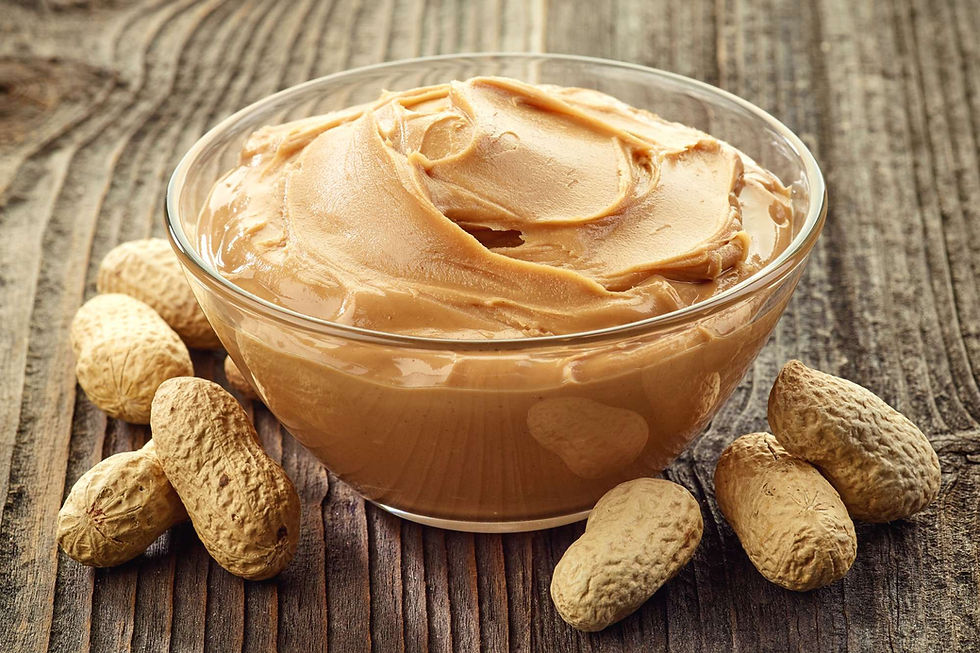 Bowl of creamy peanut butter surrounded by shelled peanuts.