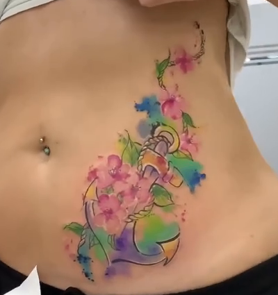 Abdominal cover-up by Laura Caselles: an anchor with rope, pink flowers and blue, green and violet watercolour