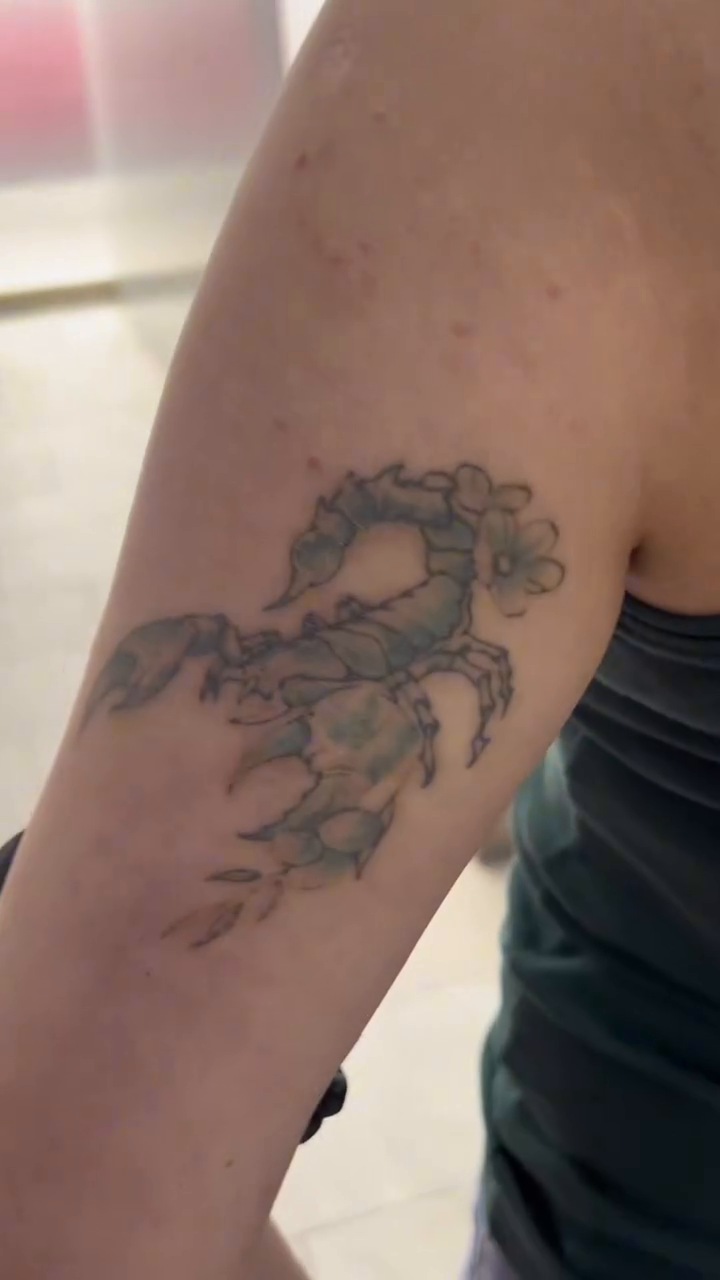 Tatuaje de escorpión oscuro y verdoso en el brazo antes del cover-up floral