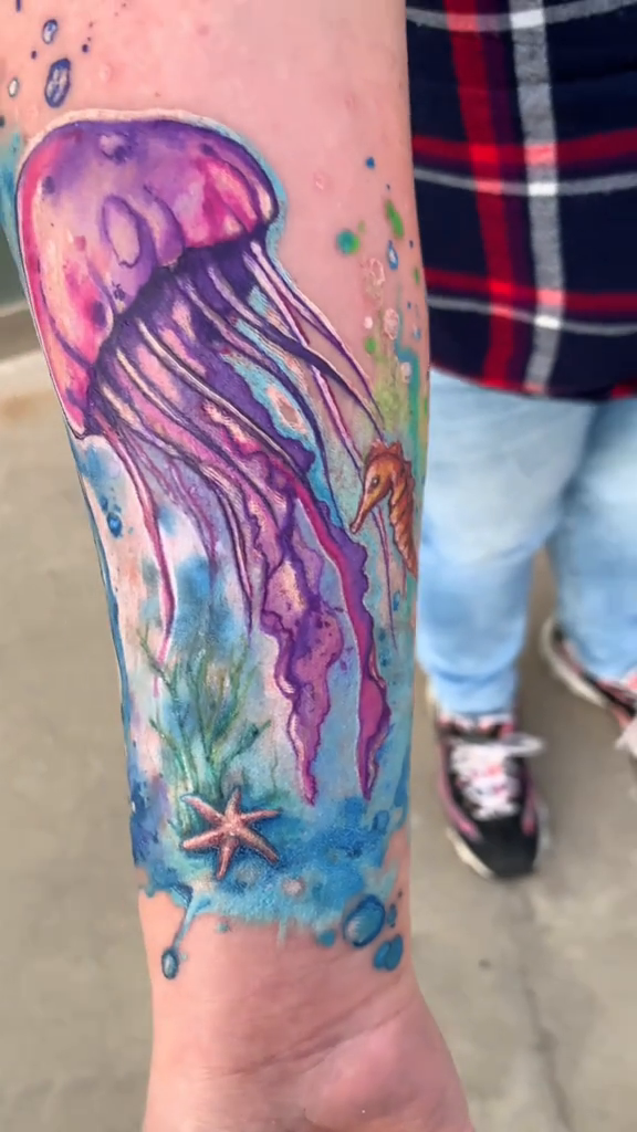 Resultado del cover-up: medusa rosa y morada, caballito de mar, burbujas y estrella de mar sobre un fondo azul en el antebrazo