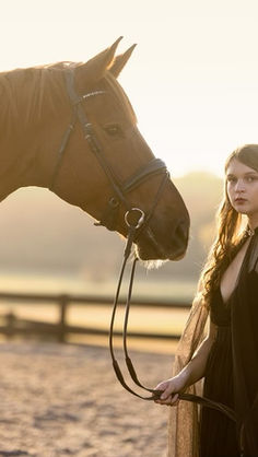 Lauren Elizabeth Pye in a sunlit photo of her in a back cape and her horse Manny