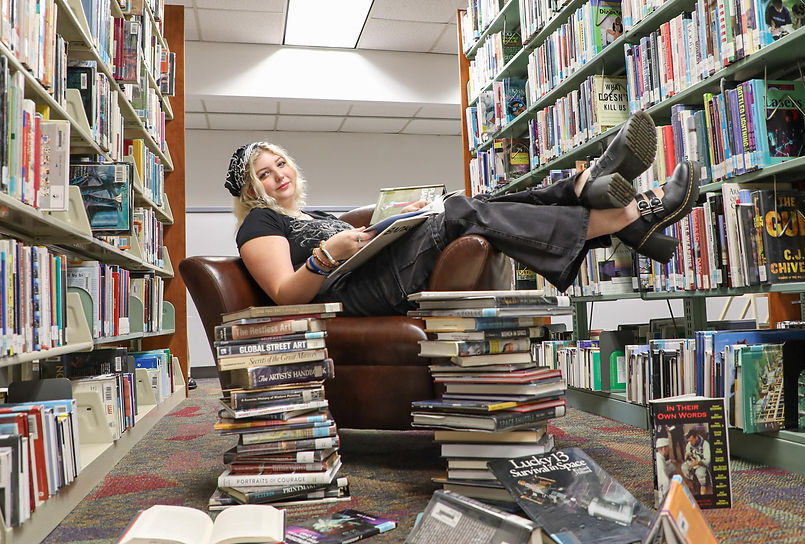 A picture of stage Manager Wren Robbins sitting on a chair surrounded by books and stacks