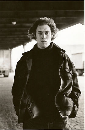 Fred Gordon aka Fred Jay Gordon, NYC based playwright, thriller / mystery novelist,  under a bridge, hands in pockets, pensive look toward the camera, 1970s