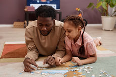 Father and young daughter assembling a jigsaw puzzle together on the floor at home.