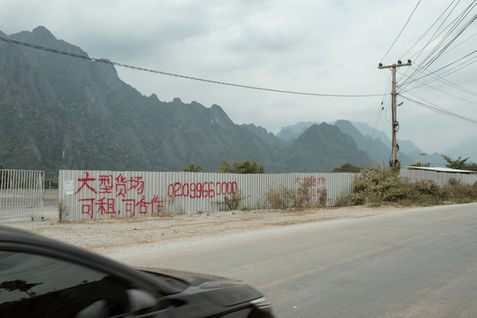 Advertisment for renting parking space for Chinese cargo trucks by the side of National Road 13 North in Vang Vieng District. The road is the main artery of Laos, stretching from Boten at the Chinese border, all the way to Vientiane Capital on the shores of the Mekong River. Originally constructed with assistance from French colonial powers during the early 20th century, this historic route has played a pivotal role in connecting diverse regions, facilitating trade, transportation, and the movement of people across Laos. Over the years, it has witnessed significant changes, becoming a crucial lifeline for the nation’s economic and cultural exchange.