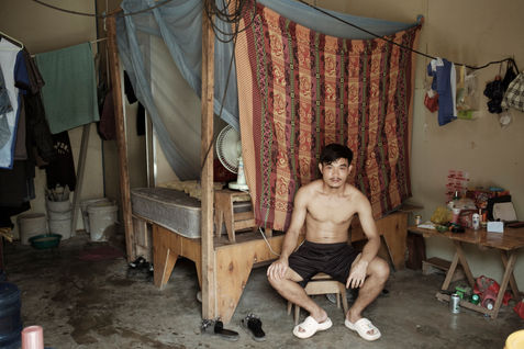 A Lao construction worker employed by a Chinese construction company inside his
room in Boten. Boten, located along the Lao-China border, has seen rapid development due
to its close ties with Chinese investments and infrastructure projects, such as the Lao-China
Railway. Daily wages for construction workers in Boten can be significantly higher compared
to other parts of Laos, drawing laborers from across the country. However, despite the higher
pay, working conditions can be challenging, with long hours and limited housing options. This
influx of Chinese-led construction projects has transformed the area into a hub of economic
activity, bringing various socio-economic and cultural challenges to the local community. Laos,
May 2023.
