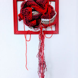 Foto des Kunstwerks mit einem aus rotem, weißen und beigem Garn gehäkelten Gehirns, das in einen roten Rahmen gespannt ist. Lose Fäden hängen nach unten aus dem Rahmen.