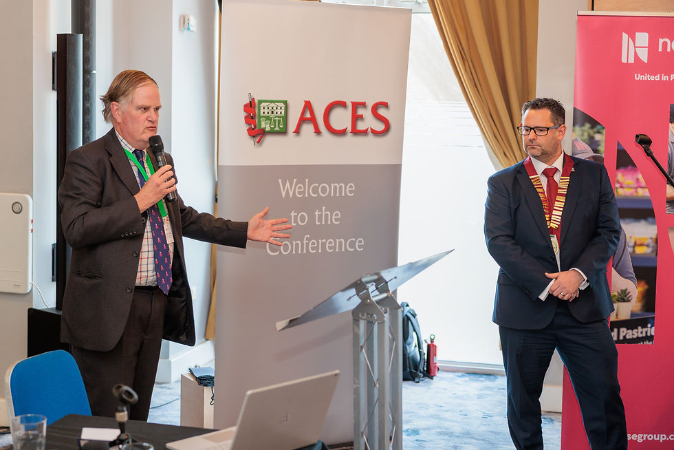 Andrew Stirling speaking into a handheld microphone beside ACES President Alan Richards during the conference closing remarks