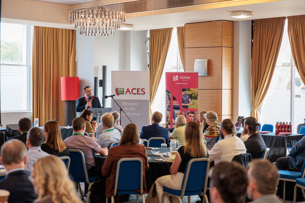 Wide view of the ACES National Conference hall with Alan Richards at the podium addressing seated delegates