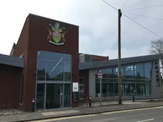 Exterior of a modern brick and glass community hub building featuring a library and civic crest.