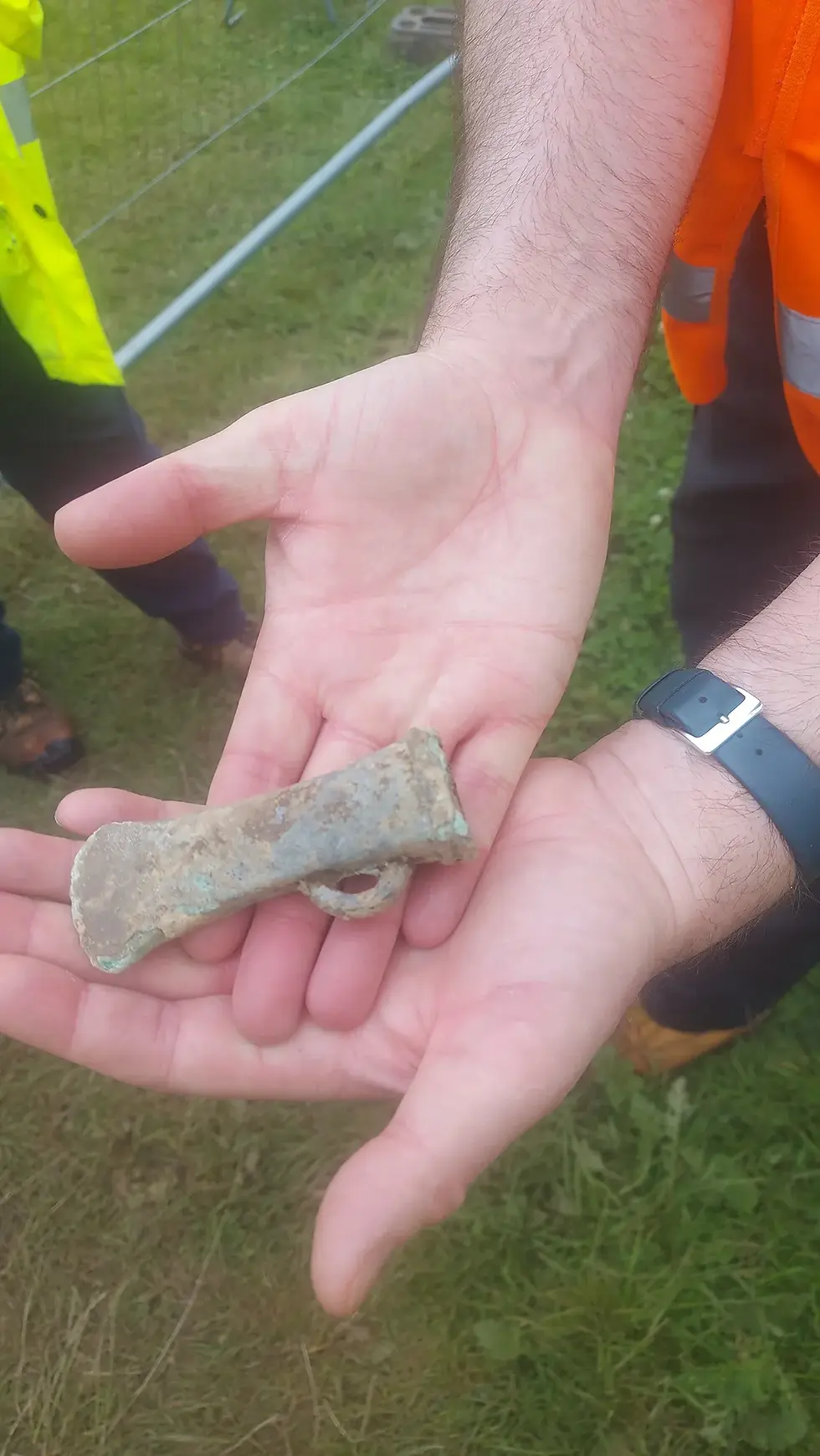 A person holding an ancient, corroded metal socketed axe head with a small loop in their open palms.