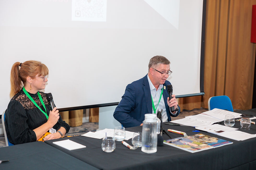 Dan Meek and Philippa Bancroft seated at a conference table with microphones during a fireside chat session on surveyor wellbeing.