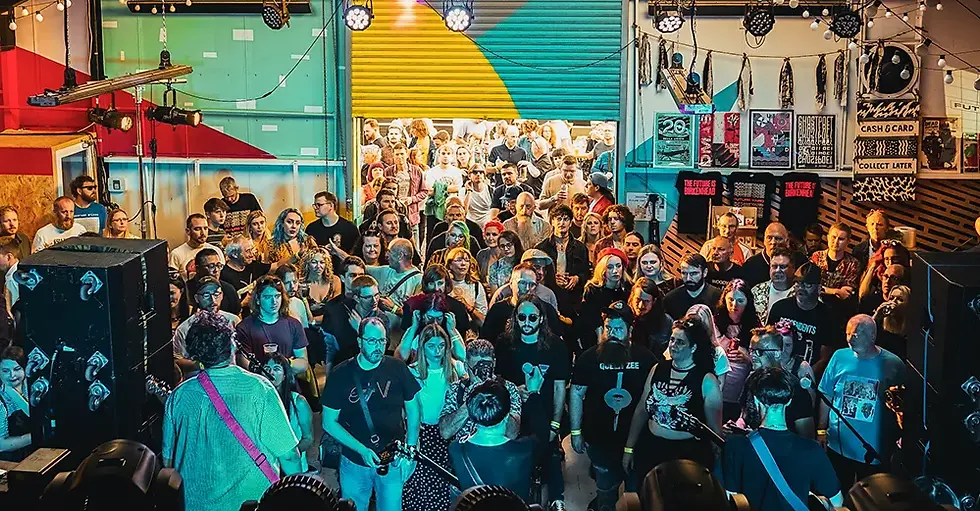 High-angle shot of a dense crowd watching a live band perform inside an eclectic indoor music venue with colorful walls.