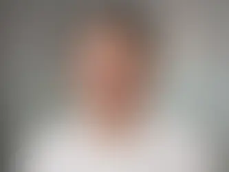 Professional close-up headshot of Chris Grose smiling, wearing glasses and a short-sleeved white button-down dress shirt against a softly blurred grey background.