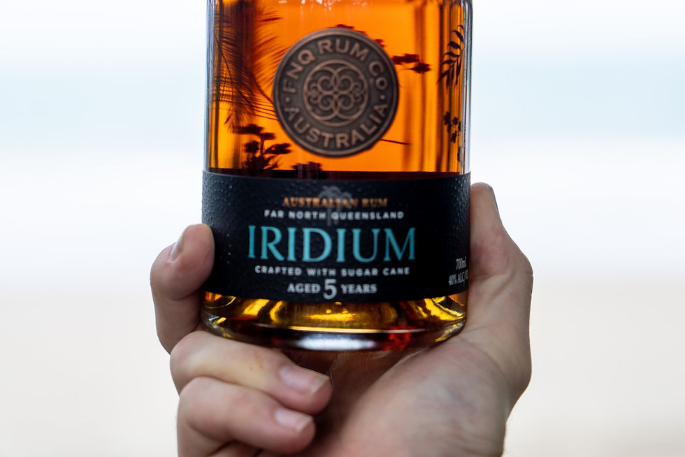 A bottle of FNQ Rum Co. Iridium 5yr Dark Rum held up to the light, showing the colour of the rum