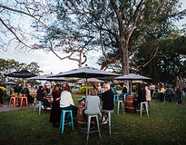 Guests seated at barrel tables under Mt Uncle Distillery umbrellas on the lawn