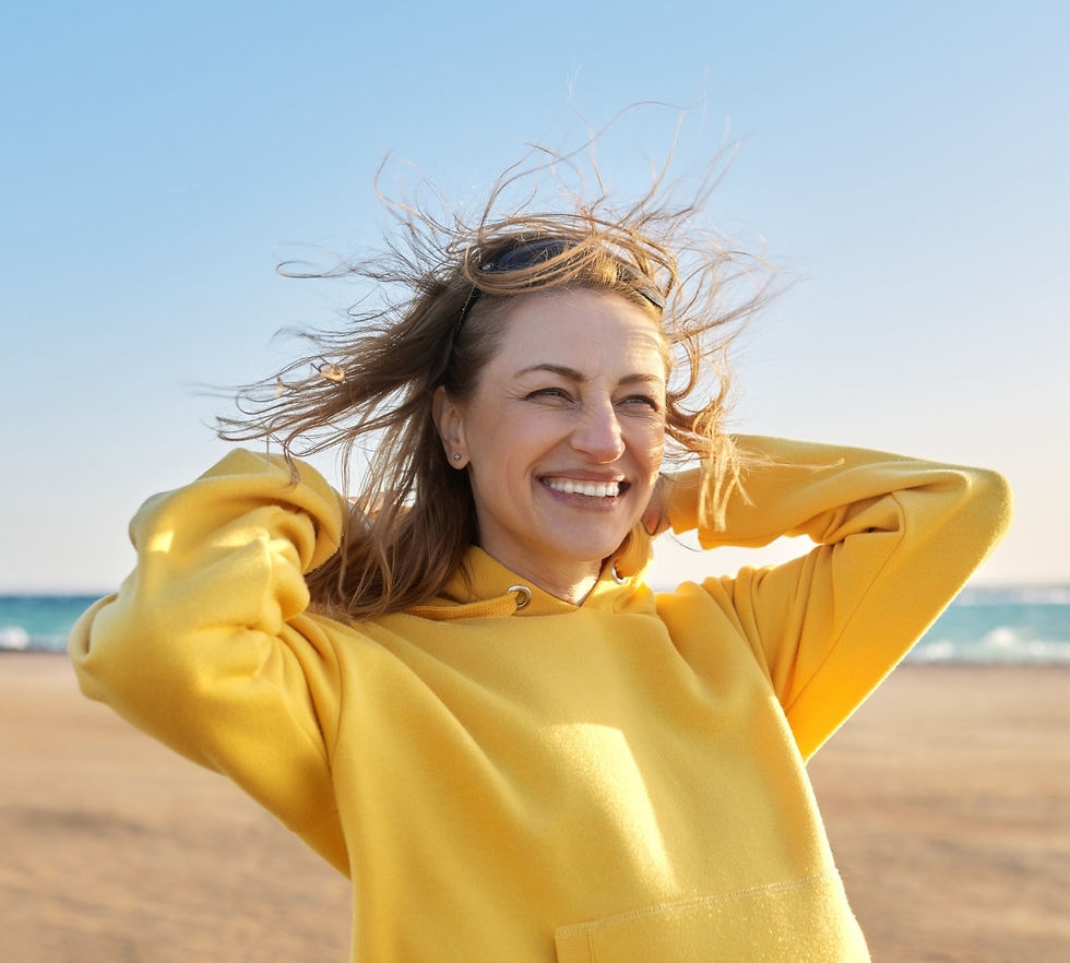 Smiling woman in a yellow hoodie enjoying the beach, feeling healthy and energized during perimenopause