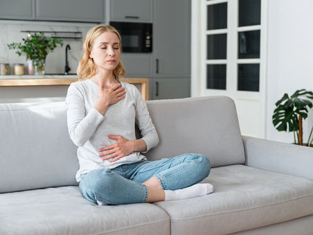 A mindful young woman with eyes closed places her hands on her chest and stomach, focusing on slow, calm breathing.