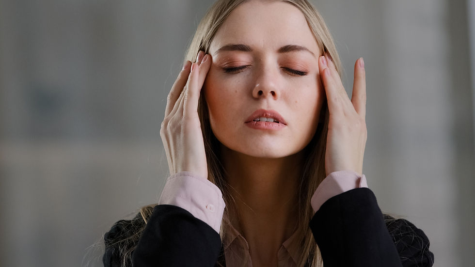 Young woman practicing self-care by relieving stress, with her fingers placed on her temples to ease tension.
