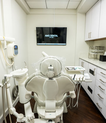 AMG Dental treatment room featuring modern dental chair, overhead light, monitor, cabinetry, and clean professional surroundings.