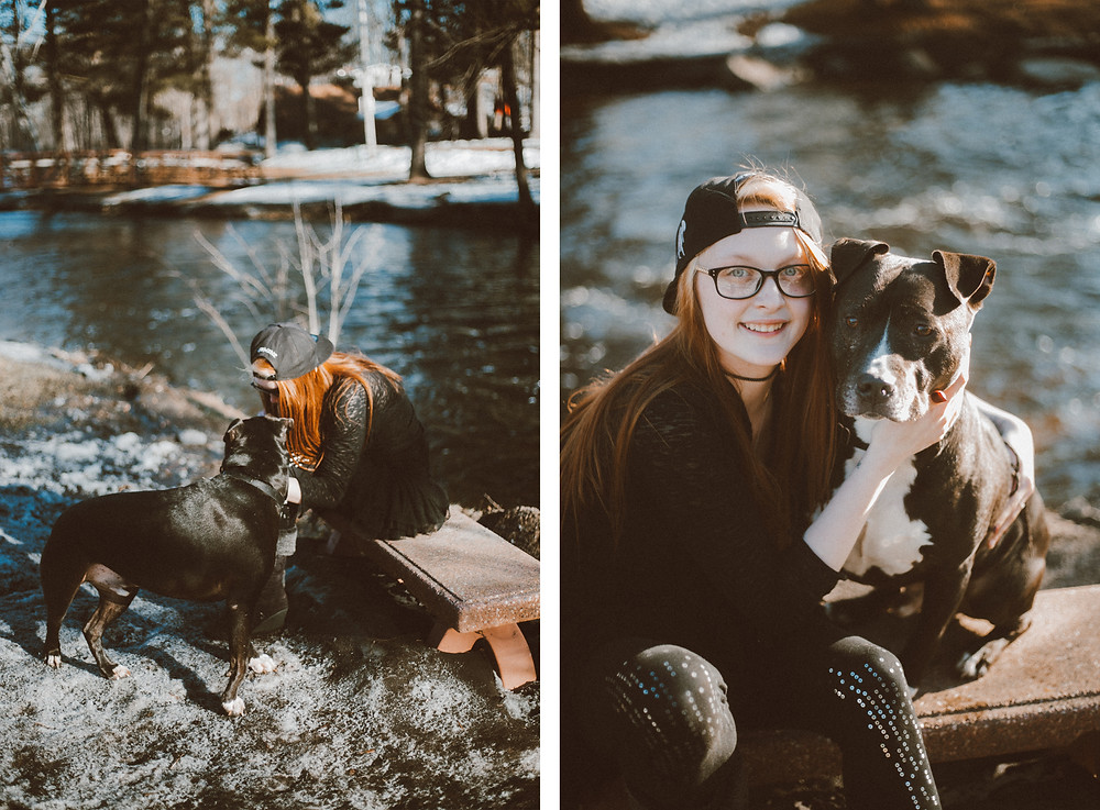 Red haired woman sits on a bench with black pitbull dog on leash during their lifestyle photography session.