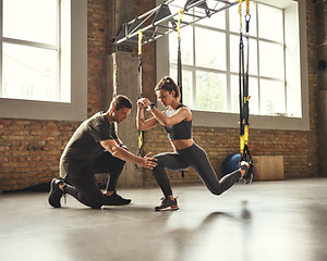 Doing squat exercise. Confident young personal trainer is showing slim athletic woman how