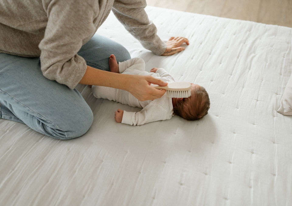 Mutter bürstet sanft die Haare ihres Neugeborenen beim Newbornshooting im Fotostudio