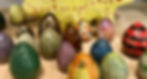 Colorful, textured ceramic eggs and a yellow, dotted figure displayed on a wooden surface. Bright and vibrant arrangement.