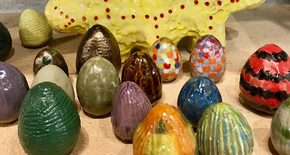 Colorful, textured ceramic eggs and a yellow, dotted figure displayed on a wooden surface. Bright and vibrant arrangement.