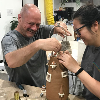 Two members happily working to wiring a hand thrown lamp base.