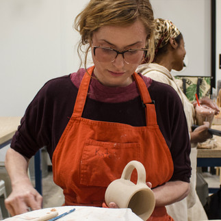 A member working to attach a handle to a mug before firing.