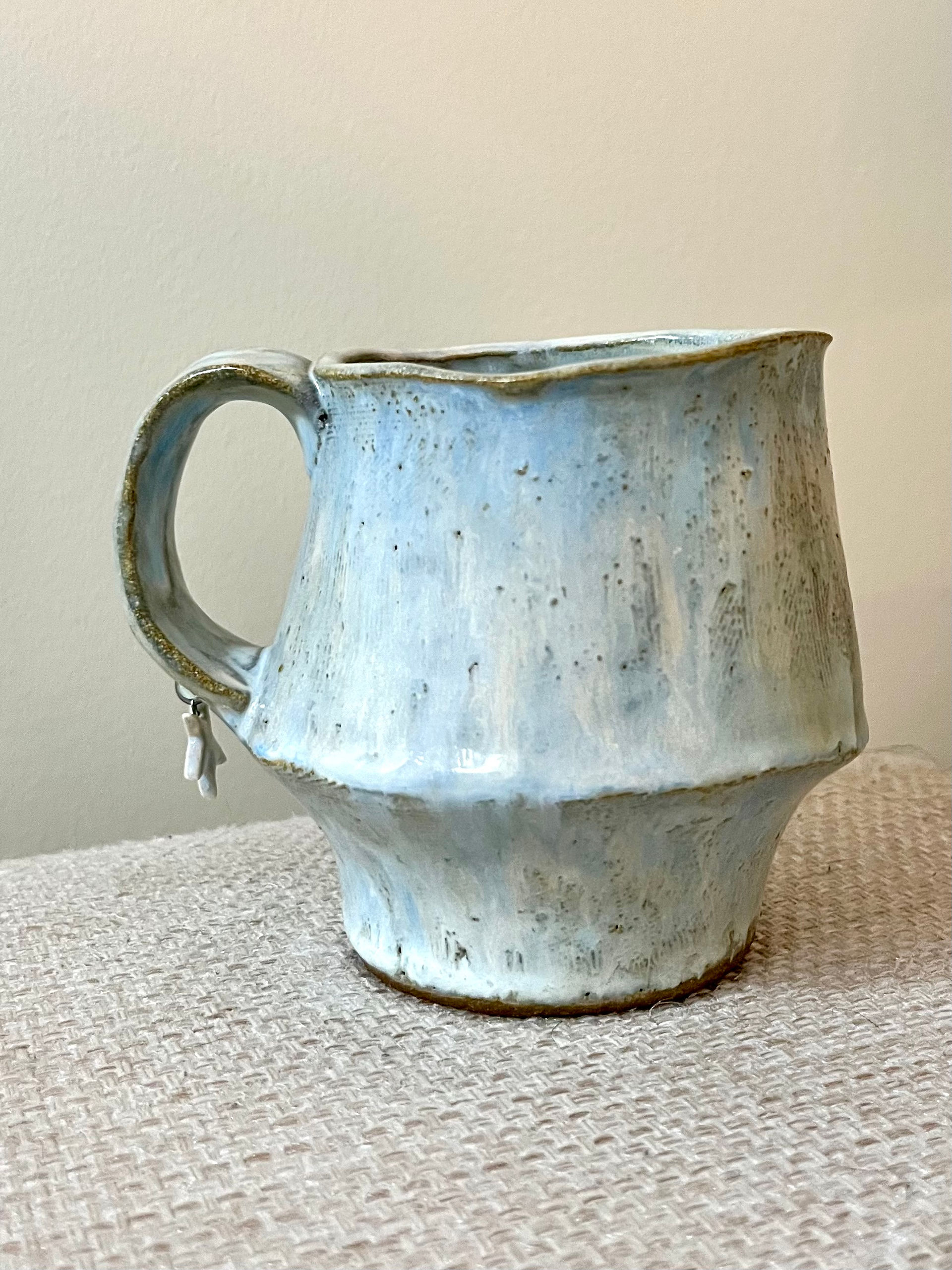 Handbuilt ceramic mug with soft curves and light blue glaze.