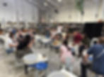 A group of pottery studio members sits gathered around a wheel demonstration at Throw Clay LA while an instructor demonstrates a ceramic technique in the center of the studio.