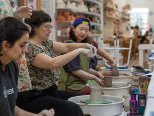 HanaKyle Moranz demonstrates body mechanics while students practice wheel throwing during a pottery workshop.